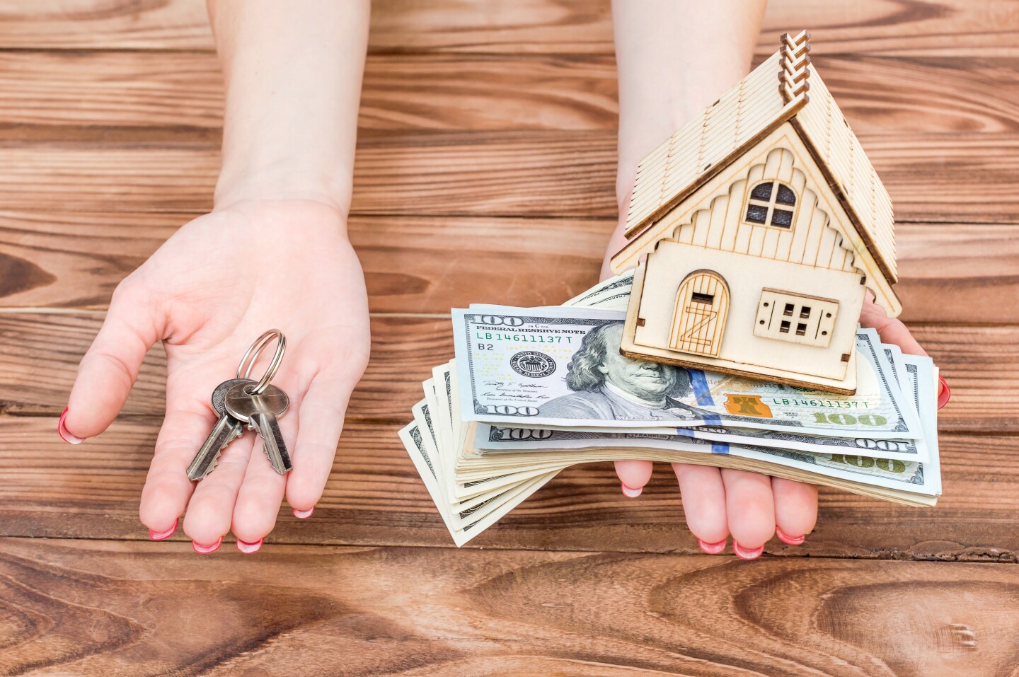 Woman's hands holding money, model of house and keys of house in palms over wooden table.