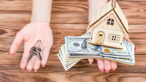 Woman's hands holding money, model of house and keys of house in palms over wooden table.